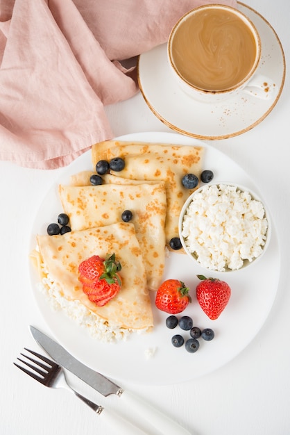 Traditional Russian thin pancakes with cottage cheese and berries in a plate on a white, top view