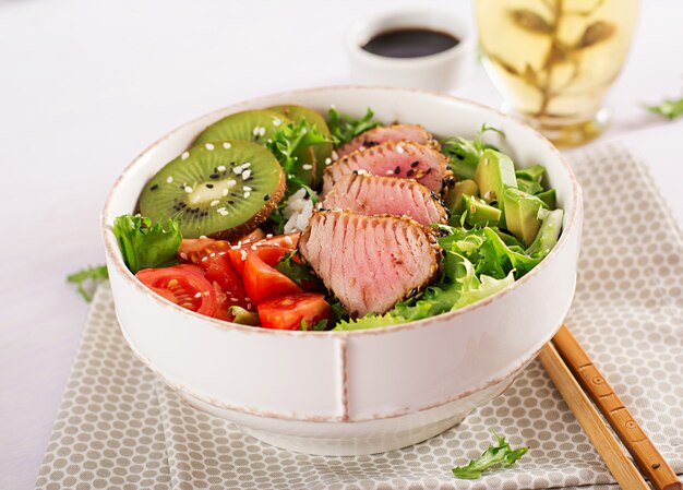Традиционный салат с кусочками средне-редкого жареного тунца Ахи и кунжута со свежими овощами и рисом на тарелке.