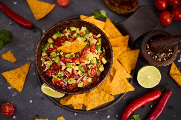 Photo traditional salsa dip snack in wooden bowl and corn nacho chips on a table with ingredients