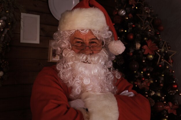 Traditional Santa Claus standing by the Christmas tree in a room.