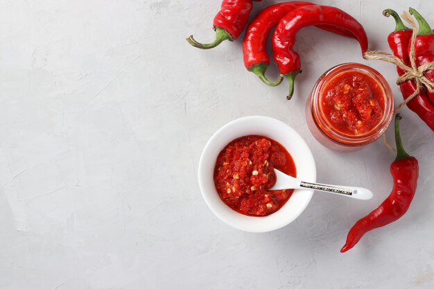 Traditional sauce adjika with hot chili pepper paste harissa on light background