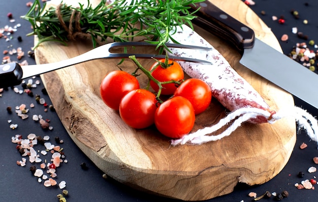 Traditional sausage with cherry tomato knife and fork with rosemary and spices on wooden cutting board