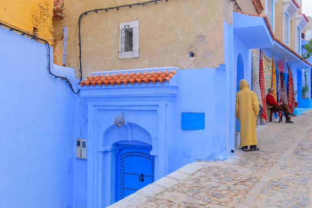 Traditional scene with people walking through street with blue painted facades of the village of Chefchaouen