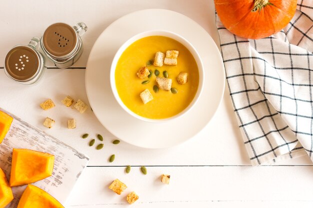 Фото Традиционный сезонный суп из тыквы в миске на деревянном белом фоне.