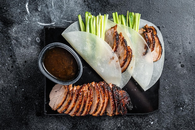 Traditional served Peking Duck with cucumber green onion in wheaten chinese pancakes Black background Top view