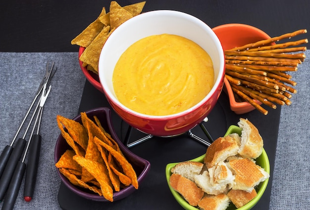 Photo traditional set  for cheese fondue with bread baguette cheese nachos and salt sticks pretzel