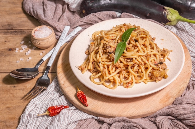 Traditional Sicilian pasta dish of sauteed eggplant topped with tomato sauce. Food served on a ceramic plate, Italian cuisine, modern hard light, dark shadow. Wooden table background, close up