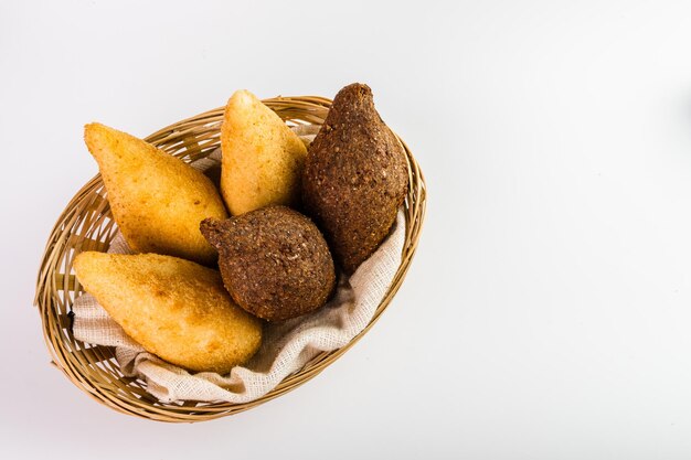 브라질의 Coxinha로 알려진 전통 스낵 치킨 Coxinha와 바구니에 담긴 튀긴 Kibe 흰색 배경 선택적 포커스