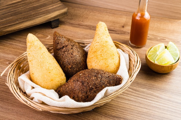 Traditional snacks Chicken Coxinha known as Coxinha in Brazil and Fried Kibe Served in a basket with spices like lemon and pepper on the side Wooden table Selective focus