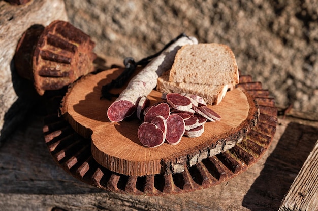 Foto fuet catalano spagnolo tradizionale tagliato a pezzi e pane a fette servito su piatto di legno su pietra con dettagli in metallo arrugginito