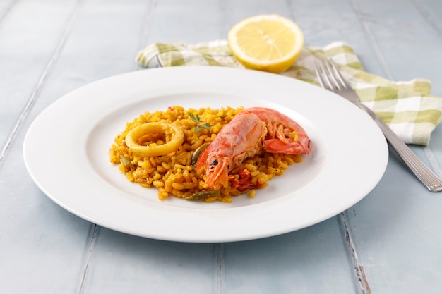 Traditional Spanish paella with seafood and vegetables served on a plate and on a blue table