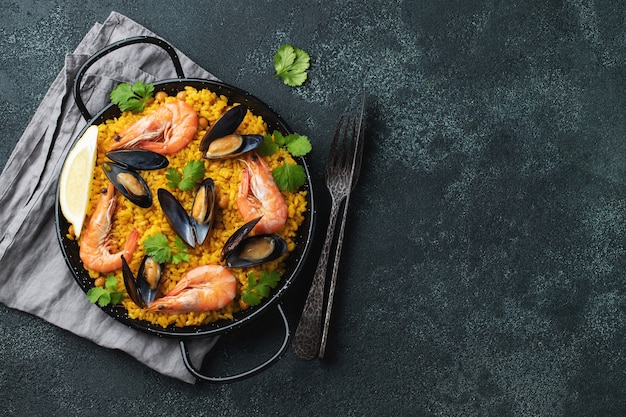traditional spanish seafood paella in a pan on elegant dark background, top view