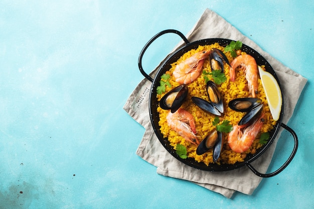 traditional spanish seafood paella in a pan on elegant light blue background, top view