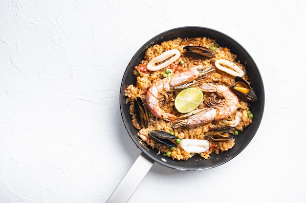 Traditional spanish seafood paella in pan on white background, top view with space for text, food photo.