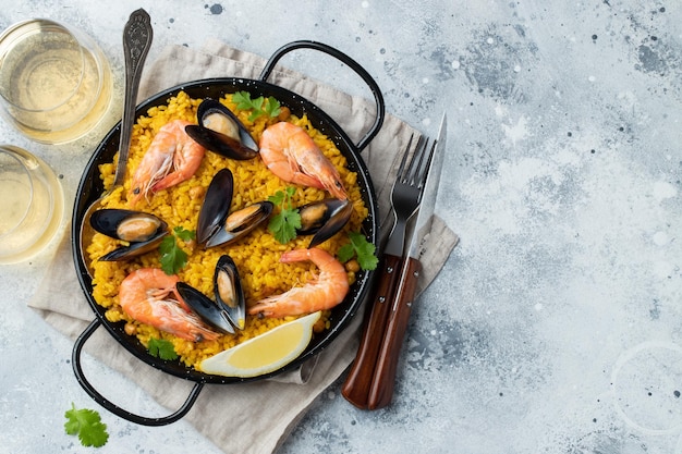 Traditional spanish seafood paella in pan with chickpeas shrimps mussels squid on light grey concrete background Top view with copy space