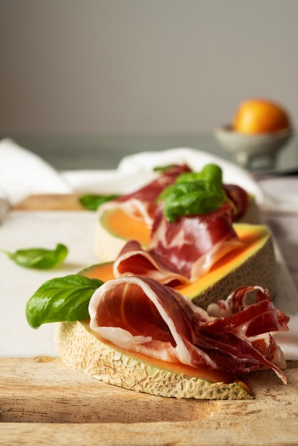 Photo traditional spanish tapas jamon iberico with basil and melon on marble serving board over pink background. top view. flat lay.