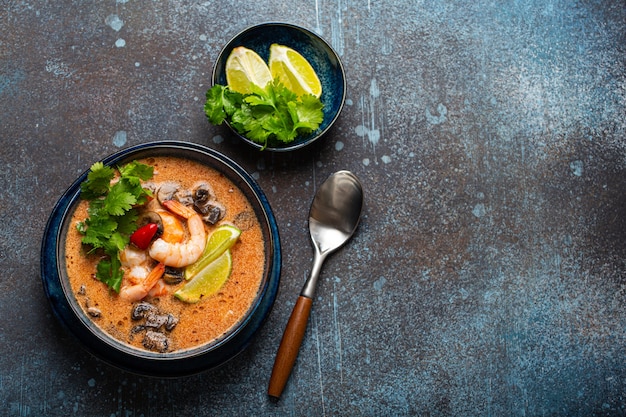 Traditional spicy Thai soup Tom Yum with shrimp and seafood in ceramic bowl on blue stone rustic background from above with space for text, classic dish of cuisine of Thailand