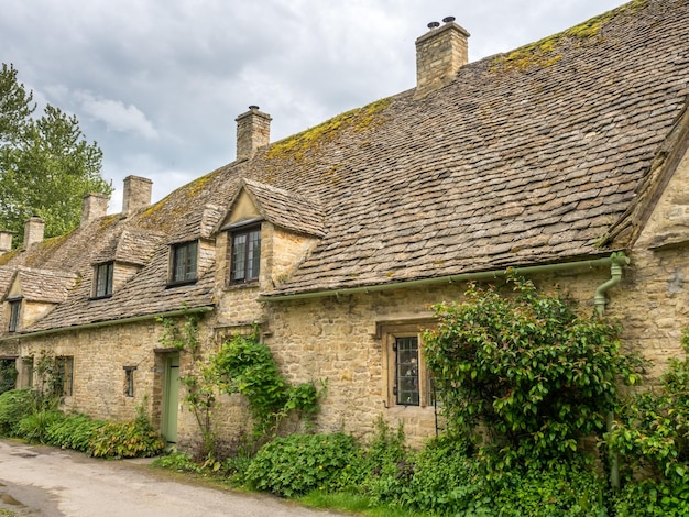 Traditional stone cottages in the peaceful cotswold village of\
bibury england under cloudy sky