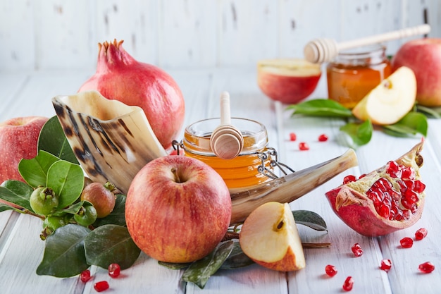 Traditional symbols: Honey jar and fresh apples with pomegranate and shofar- horn on white wooden. 