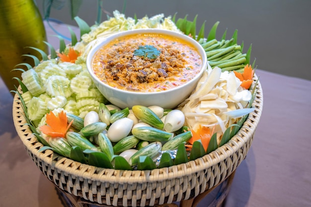 Традиционный тайский острый соус чили под названием Нам Прик в белой миске посреди овощной капусты, огурца, моркови, баклажана, чечевицы, имбиря