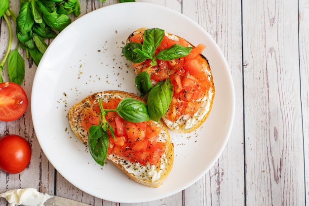 Traditional toasted Italian tomato bruschetta with spice and basil on light wooden background. Top view vith copy space.