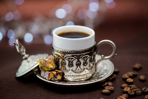 Traditional Turkish coffee in traditional metal cup on brown table with Turkish delight and bokeh