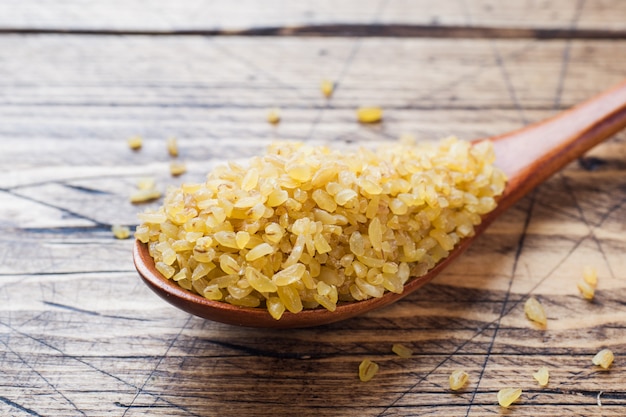 Traditional Turkish dry raw bulgur cereal in a wooden spoon.