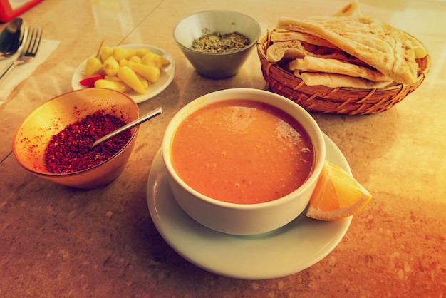 Traditional turkish soup with lentils on the table with bread and spicy condiments food background