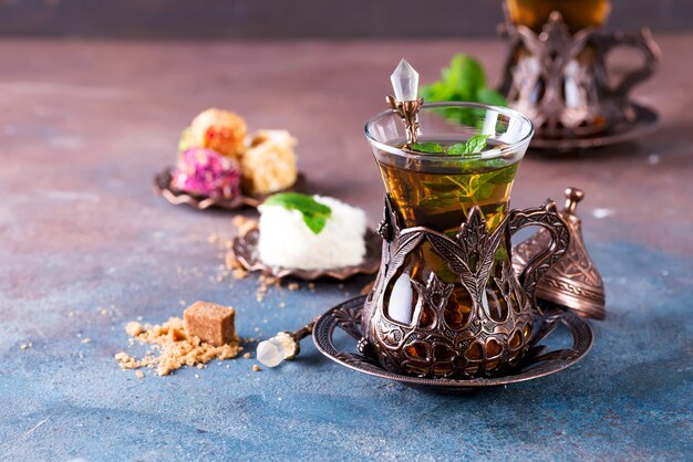 Traditional turkish tea with mint leaves and sweets in a traditional glass on concrete