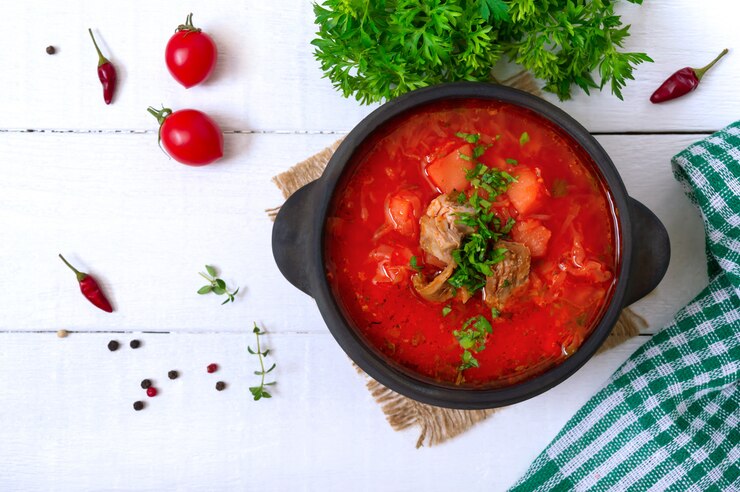 Традиционный украинский борщ с молодыми овощами и мясом в черном глиняном горшочке на белой деревянной поверхности
