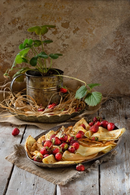 イチゴの果実と木製のテーブルの上に蜂蜜と伝統的なウクライナまたはロシアのパンケーキ
