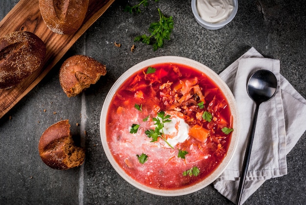 Traditional Ukrainian Russian vegetable soup borscht, with hard cream. parsley rye bread rolls, on black stone table, copy space top view