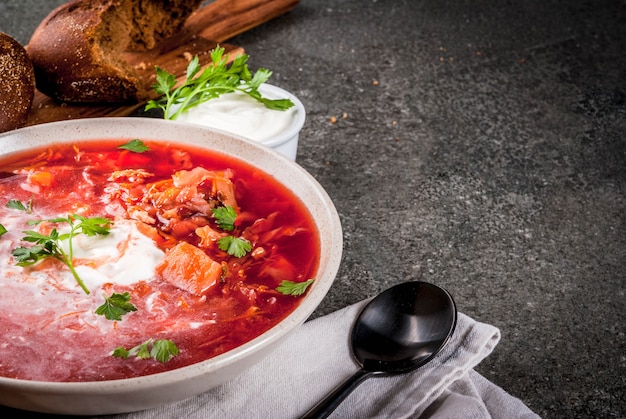 Traditional Ukrainian Russian vegetable soup borscht, with hard cream. parsley rye bread rolls, on black stone table, copy space