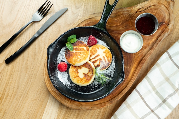 Traditional Ukrainian syrniki. pancakes with cottage cheese in a pan with sour cream and jam on a wooden board.