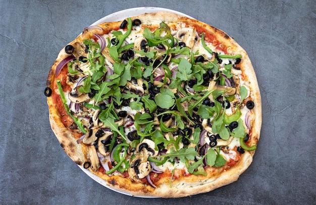 Traditional vegetable pizza with arugula on rustic table top view