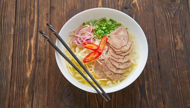 Traditional Vietnamese soup Pho bo with meat, rice noodles, asian soup in bowl with chopsticks. Space for text. Top view. Asian soup Pho bo on wooden table background.