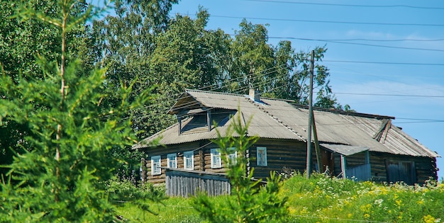 Casa di villaggio tradizionale sullo sfondo di un paesaggio estivo di erba e cielo blu, villaggio russo settentrionale