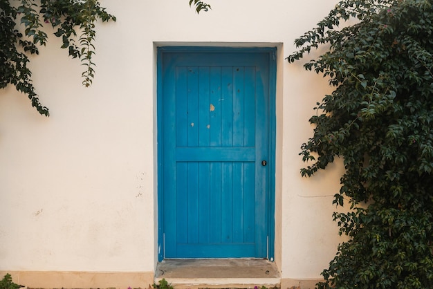 Traditional white Greek house facade with blue door Closeup of a wooden blue dors and flower in a white stone building