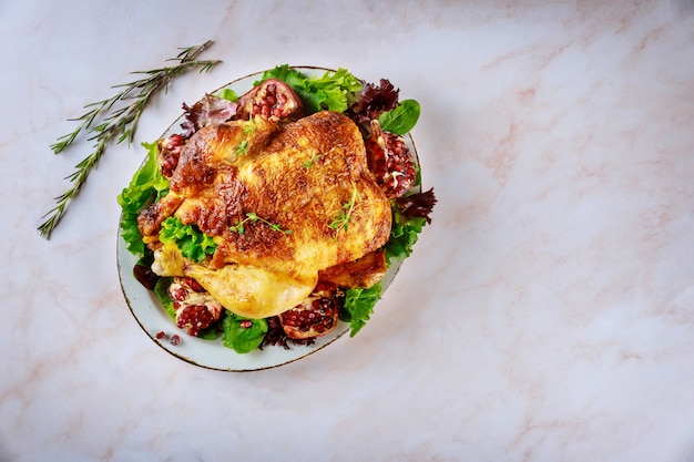 Traditional whole roasted chicken on plate with pomegranate, rosemary and green salad.