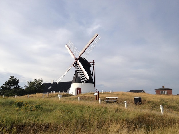 Traditional windmill on grassy field against sky