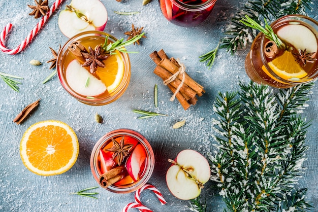 Traditional winter drinks, white and red mulled wine cocktail,  with white and red wine, spices, apple, orange. On a light blue table,