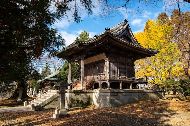 Traditional wooden Japanese temple with written prayers, autumn trees, blue sky.