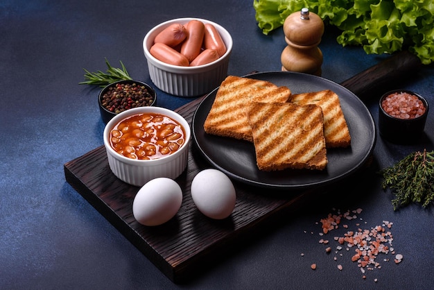 Traditioneel Engels ontbijt met eieren toast worstjes bonen specerijen en kruiden op een grijze keramische plaat