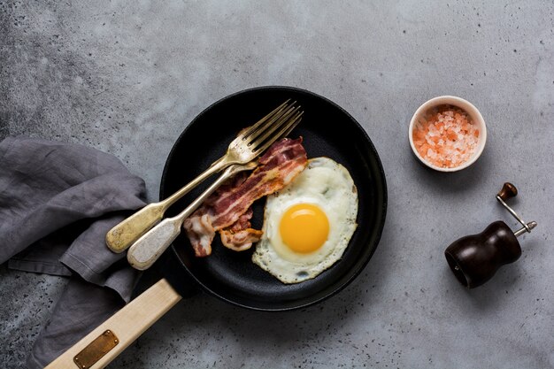 Traditioneel Engels ontbijt met gebakken eieren en spek in gietijzeren pan op oude grijze betonnen ondergrond. Bovenaanzicht.