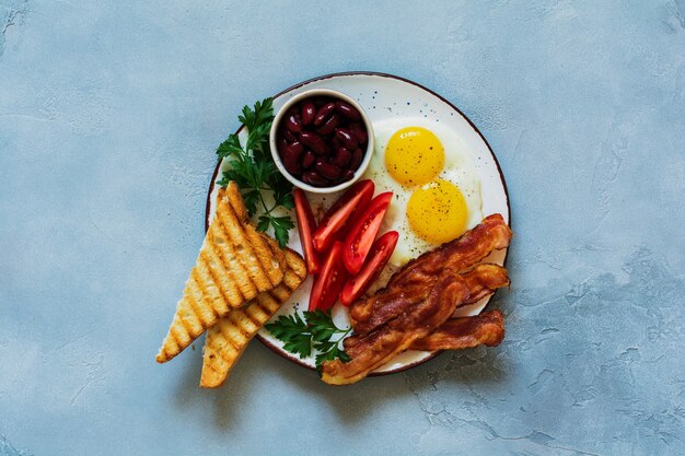 Traditioneel Engels ontbijt met gebakken eieren, spek, bonen, toast en tomaten op grijs beton