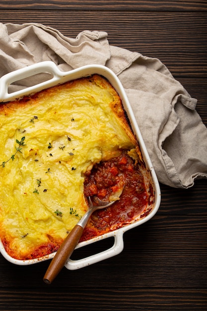 Traditioneel gerecht uit de Britse keuken Shepherd's pie braadpan met gehakt en aardappelpuree in keramische ovenschaal op witte rustieke tafel met lepel van bovenaf