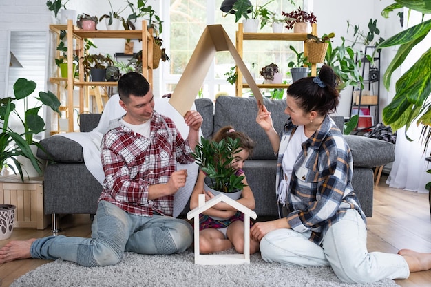 Traditioneel gezin met kind geniet van nieuw huis, zittend op de bank en houdt het dak vast Hypotheekverzekering en bescherming kopen en verhuizen naar uw eigen groene huis met potplant