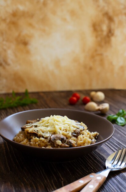 Traditioneel Italiaans gerecht van risotto van rijstarborio met paddestoelen. Geserveerd met verse basilicum, champignons en kerstomaatjes op een donkere houten tafel. Verticaal. Detailopname. Licht marmeren achtergrond