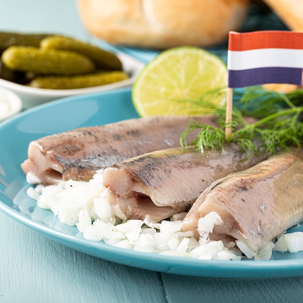 Traditioneel Nederlands eten vers gezouten haringvis met ui genaamd hollandse nieuwe op turkooizen plaat en houten oppervlak. Europees voedselconcept