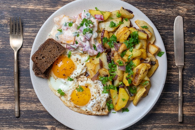 Traditioneel Oekraïens eten, gebakken aardappelen met uien, gebakken eieren, groentesalade, zwart brood op houten achtergrond, close-up, bovenaanzicht